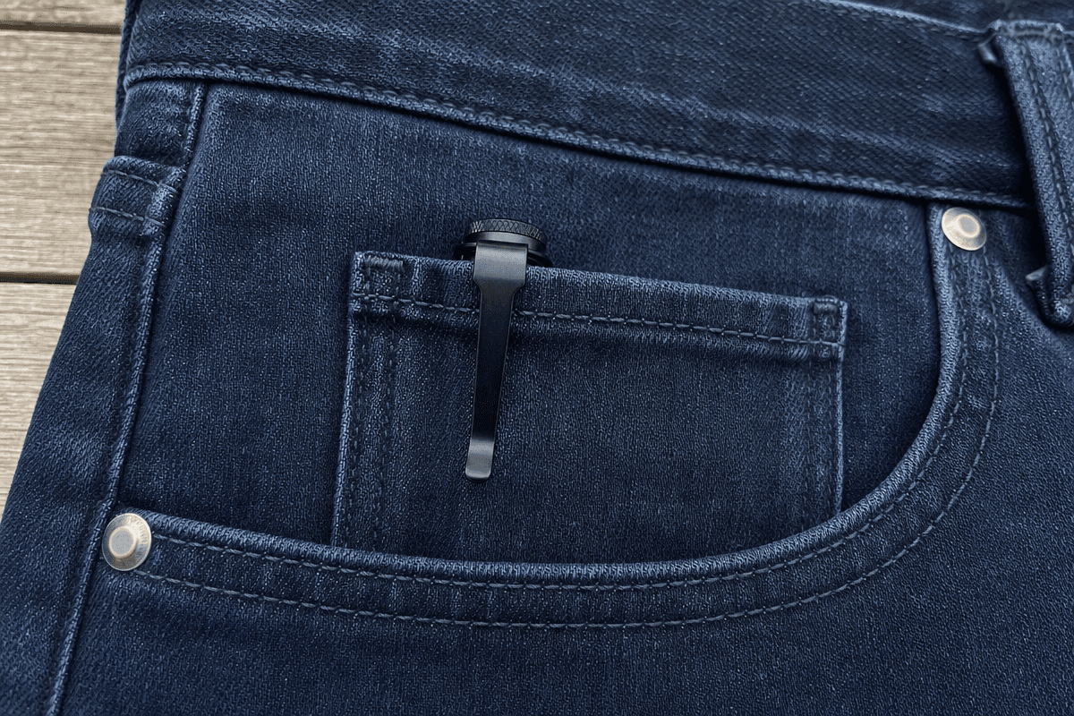 A small flashlight clipped inside the coin pocket of dark jeans — barely visible, zero printing